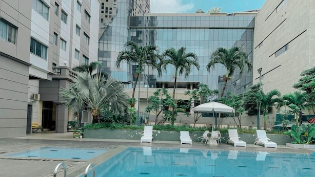 A swimming pool with lounge chairs and palm trees, surrounded by modern buildings.