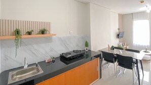 A modern kitchen with a marble countertop, a built-in sink, and a wooden shelf with plants.