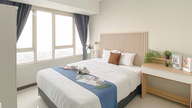 A modern bedroom with a large bed, a bedside table, a window with curtains, and a headboard.