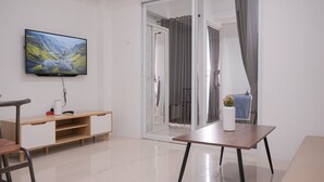 Uma sala de estar moderna com uma TV de tela plana, um armário de madeira, uma porta de vidro que dá para uma varanda e uma pequena mesa com um vaso.