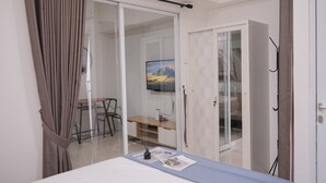 Quarto com cama, escrivaninha e cadeira. Porta de correr dá acesso a um banheiro.