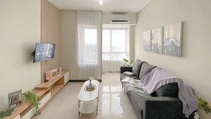 A modern living room with a flat-screen TV, a grey sofa, a coffee table, and a view of the city through large windows. - Minimalistic Designed 2Br Nifarro Park Apartment (Jakarta)
