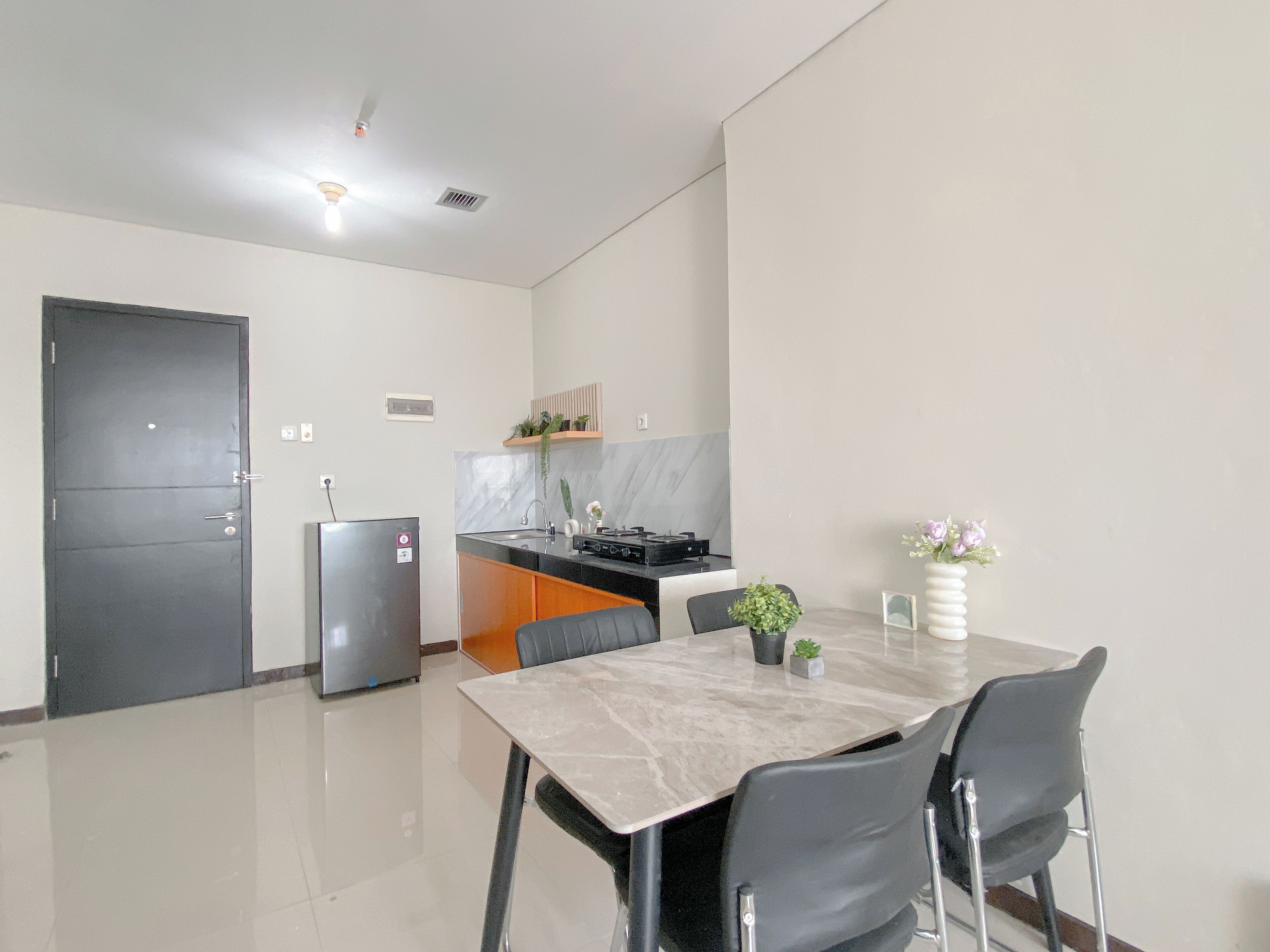 A modern kitchen with a marble countertop, a built-in oven, and a sink. There is a dining table with chairs and a potted plant on the table.