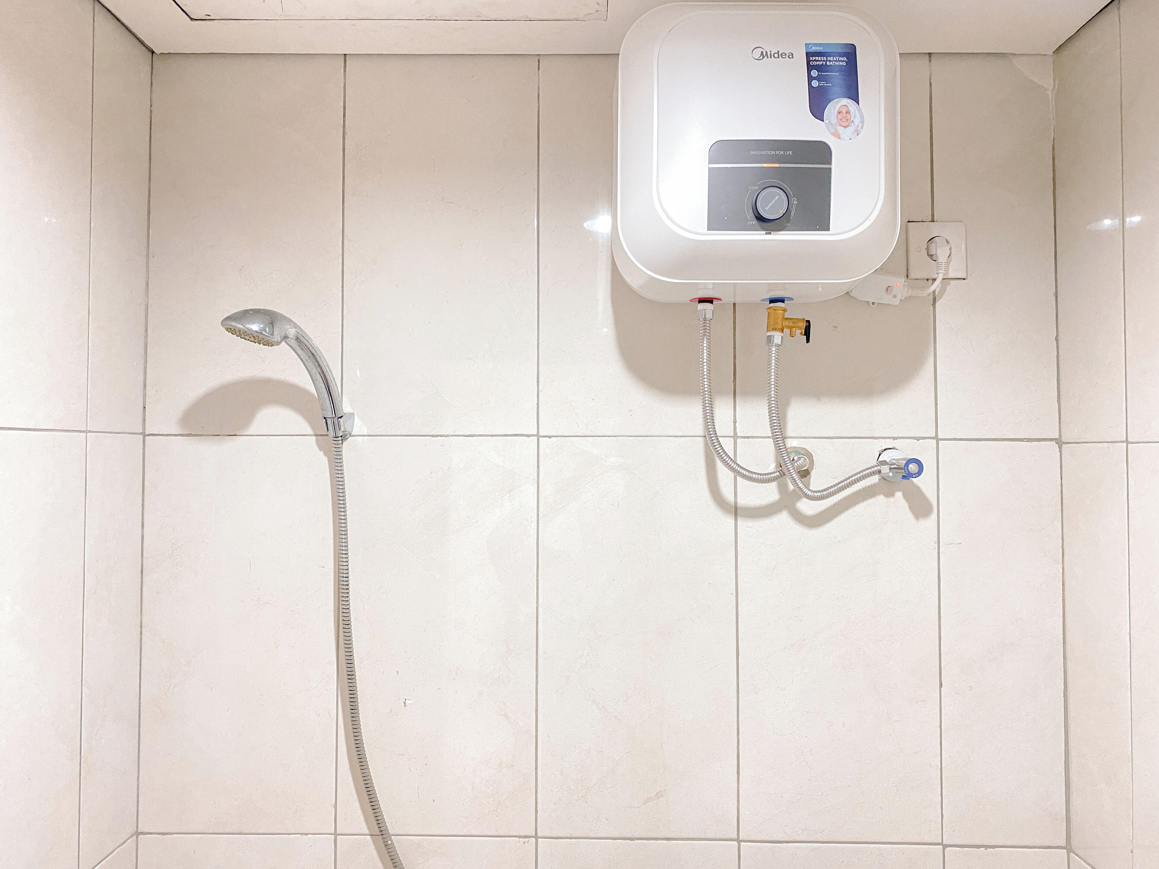 A bathroom with a white tiled wall, a showerhead, and a water heater unit.