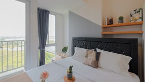 A modern bedroom with a large bed, a view of the city, and a balcony. - Comfort And Warm Studio At Tokyo Riverside Pik 2 Apartment (Teluknaga)
