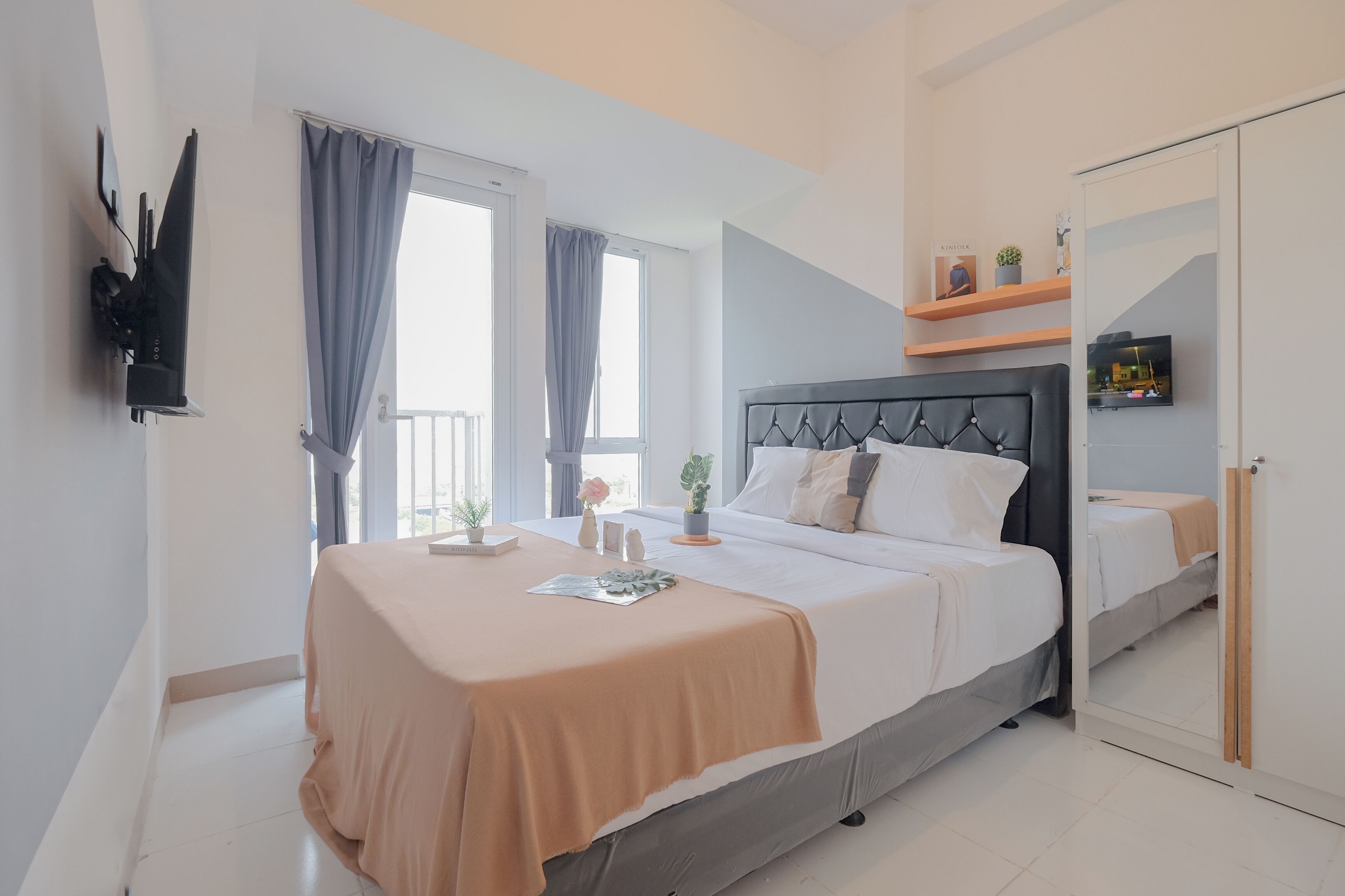 Une chambre moderne avec un grand lit, une table de chevet, un miroir et un téléviseur fixé au mur.