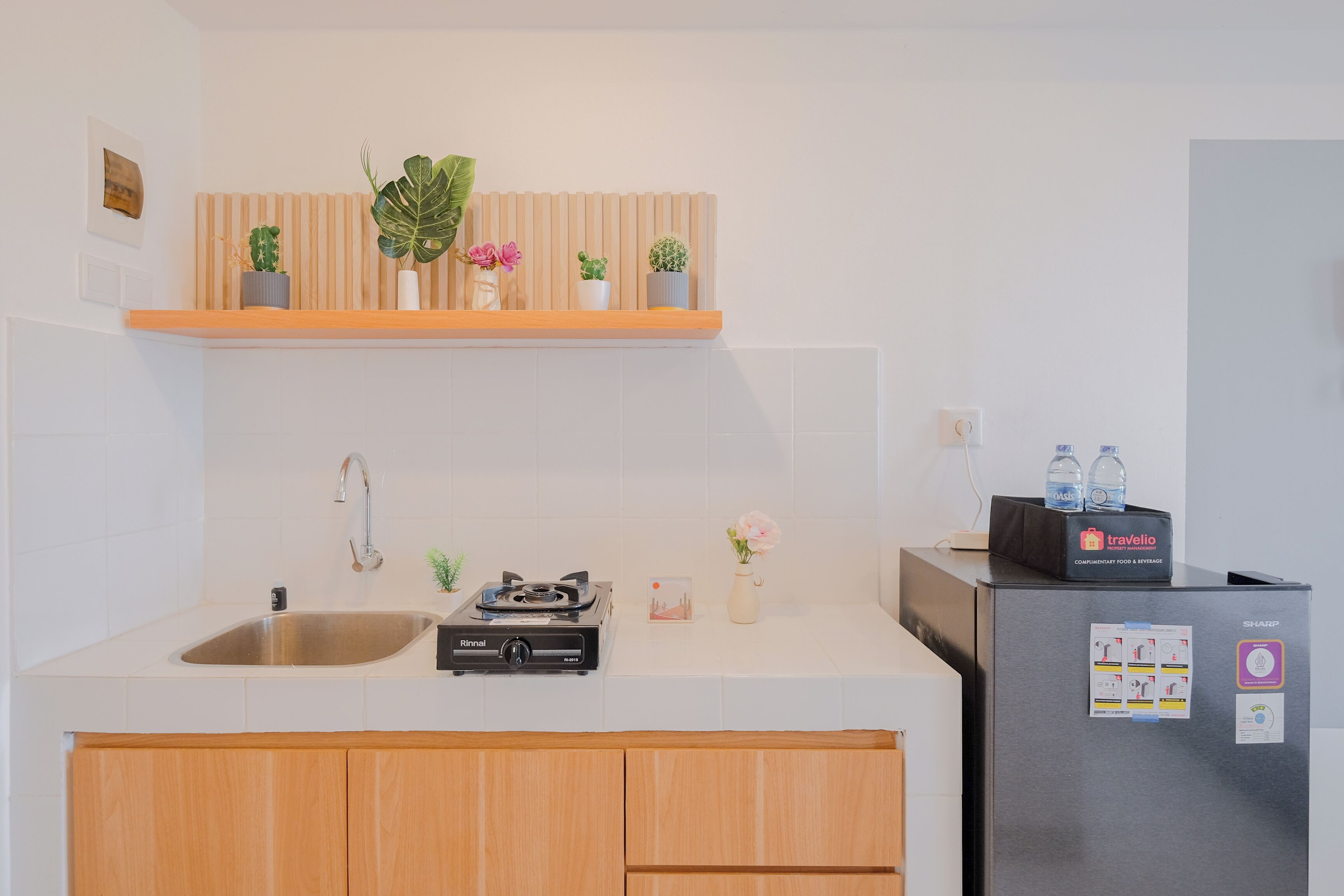 Eine moderne Küche mit Spüle aus Edelstahl, integriertem Herd, Holzschränken und einem Kühlschrank mit einem travelio Aufkleber.