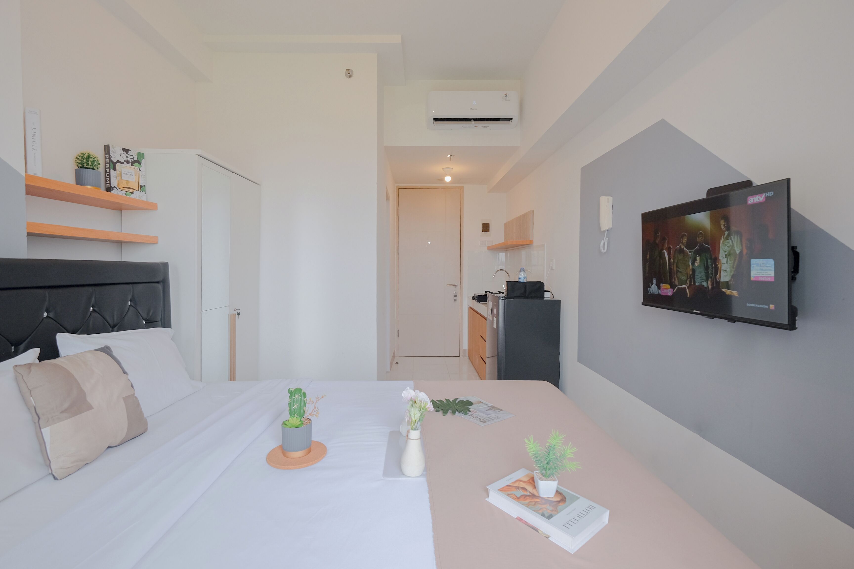 Moderni hotellihuone, jossa on sänky, yöpöytä, televisio ja pieni keittotila.