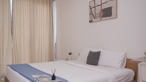Una cama bien hecha con una manta azul, una mesita de noche con lámpara y una pared con arte abstracto.