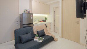 A compact living space with a sofa, a kitchenette, and a TV mounted on the wall. - Spacious And Homey Corner 2Br Tokyo Riverside Pik 2 Apartment (Teluknaga)