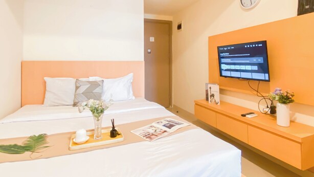 A hotel room with a bed, a TV mounted on the wall, a bedside table with a vase of flowers, and a tray with a cup and a plant.