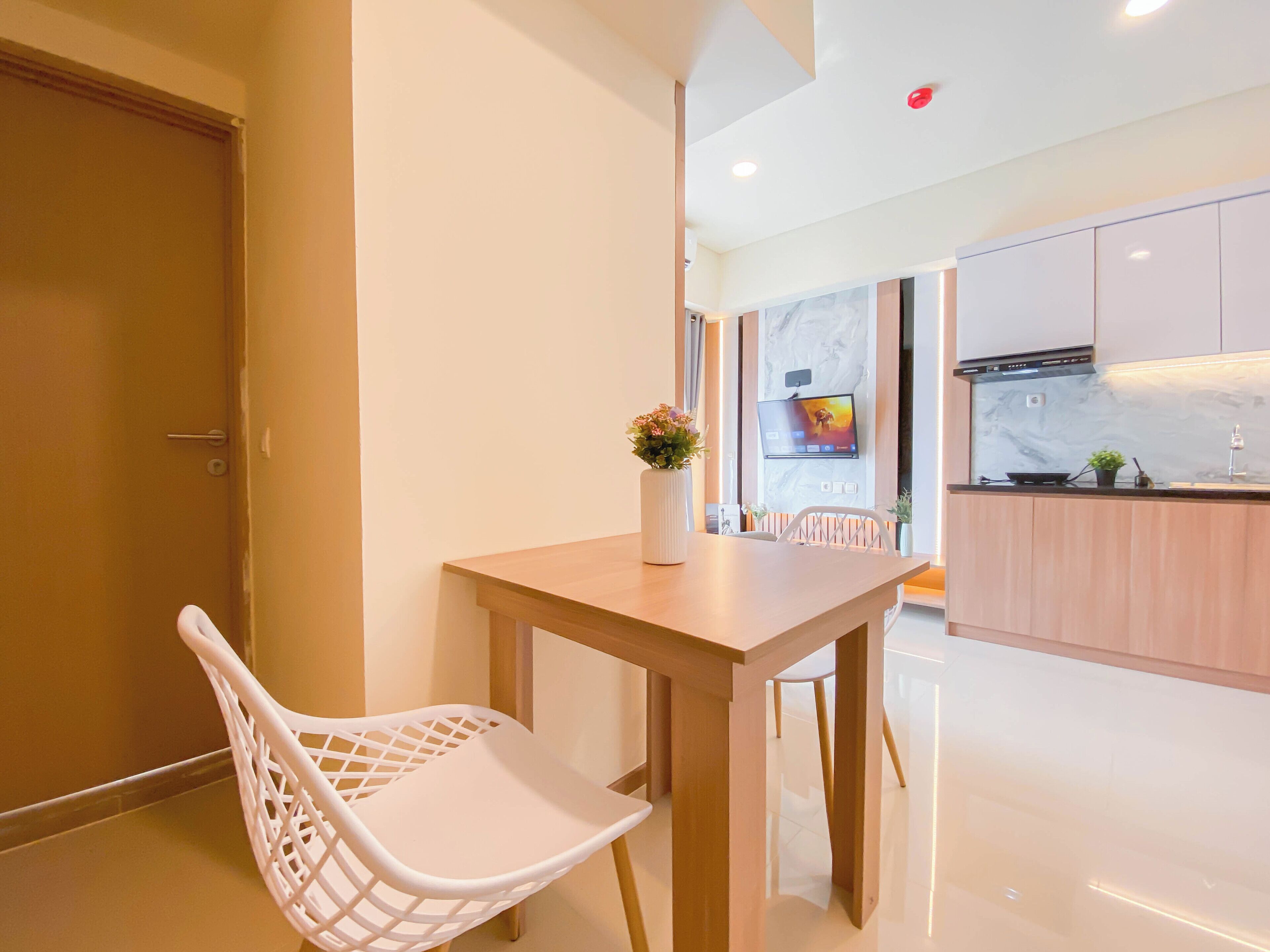 A modern kitchen with a wooden table, white chairs, a TV mounted on the wall, and a small plant on the counter.
