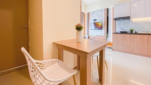 A modern kitchen with a wooden table, white chairs, a TV mounted on the wall, and a small plant on the counter. - Homey And Modern 2Br At Meikarta Apartment (Cikarang)