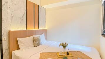 A neatly made bed with white linens, a wooden headboard, and a bedside table with a vase of flowers and a book.