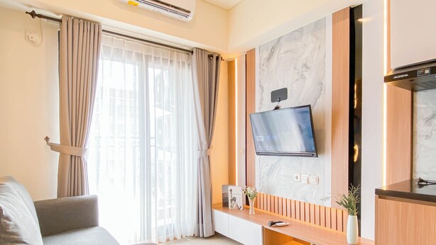 A modern living room with a flat-screen TV mounted on the wall, a sofa, and a wooden entertainment unit with a vase and a small plant. - Homey And Modern 2Br At Meikarta Apartment (Cikarang)