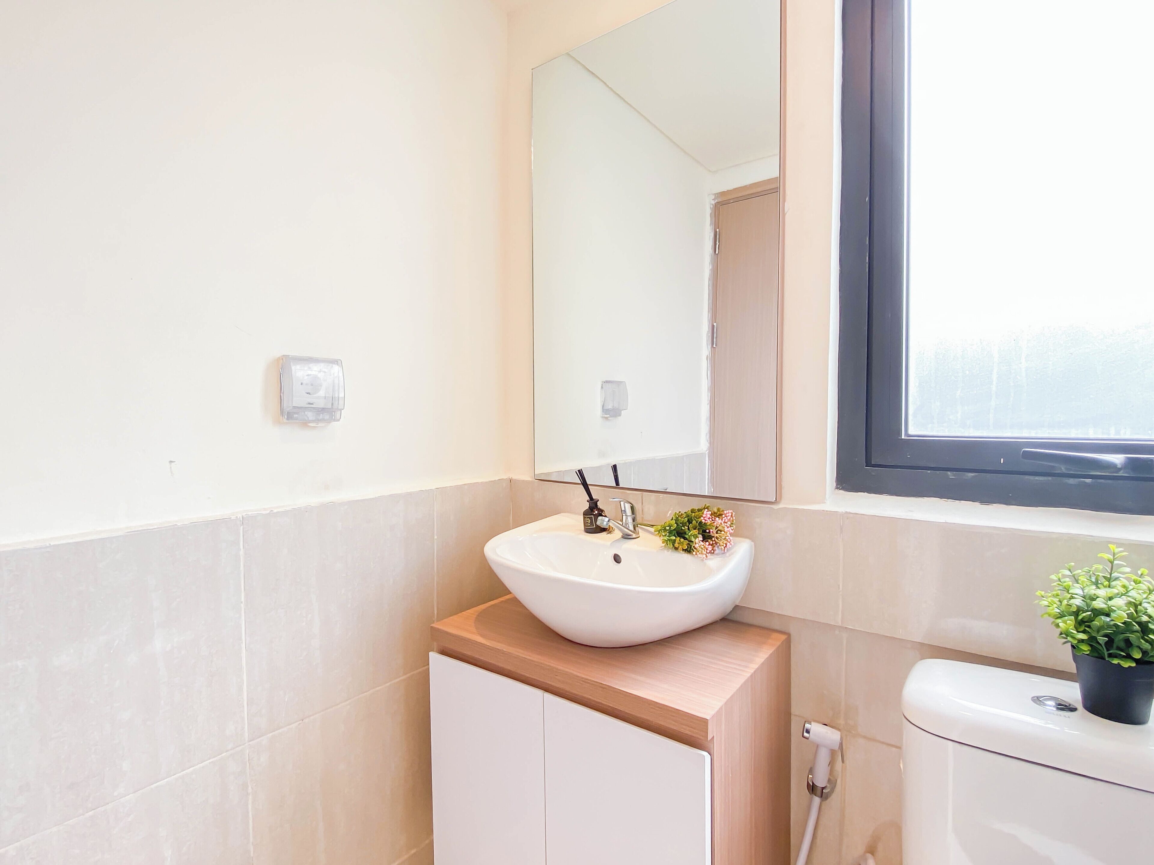 A bathroom with a white sink, a mirror, a window, and a toilet.