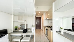A modern kitchen with a dark brown door, white cabinets, and a marble floor. There is a dining area with a white table and chairs, and a small potted plant on the counter. - Modern Look And Homey Studio At Apartment Sky House Bsd (Pagedangan)