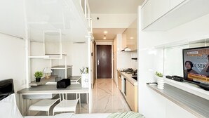 A modern kitchen with white cabinetry, a built-in stove, and a TV mounted on the wall. - Modern Look And Homey Studio At Apartment Sky House Bsd (Pagedangan)