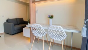 A modern living room with a sofa, a dining table with two chairs, a vase with flowers, and a ceiling light. - Best Living 2Br At Meikarta Apartment (Cikarang)