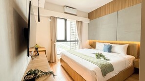 A modern hotel room with a large bed, a bedside table with a lamp, and a view of the outdoors through a window with curtains. - Spacious And Stylish 3Br At Sky House Bsd Apartment (Pagedangan)