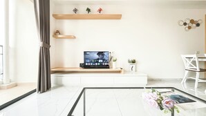 A modern living room with a flat-screen TV, a white console table, and a glass coffee table with a floral centerpiece.