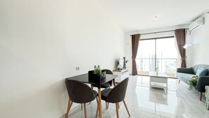 A modern living room with a dining area, large windows, and a view of the city. - Quiet And Homey 2Br With Extra Room Apartment Sky House Bsd (Pagedangan)