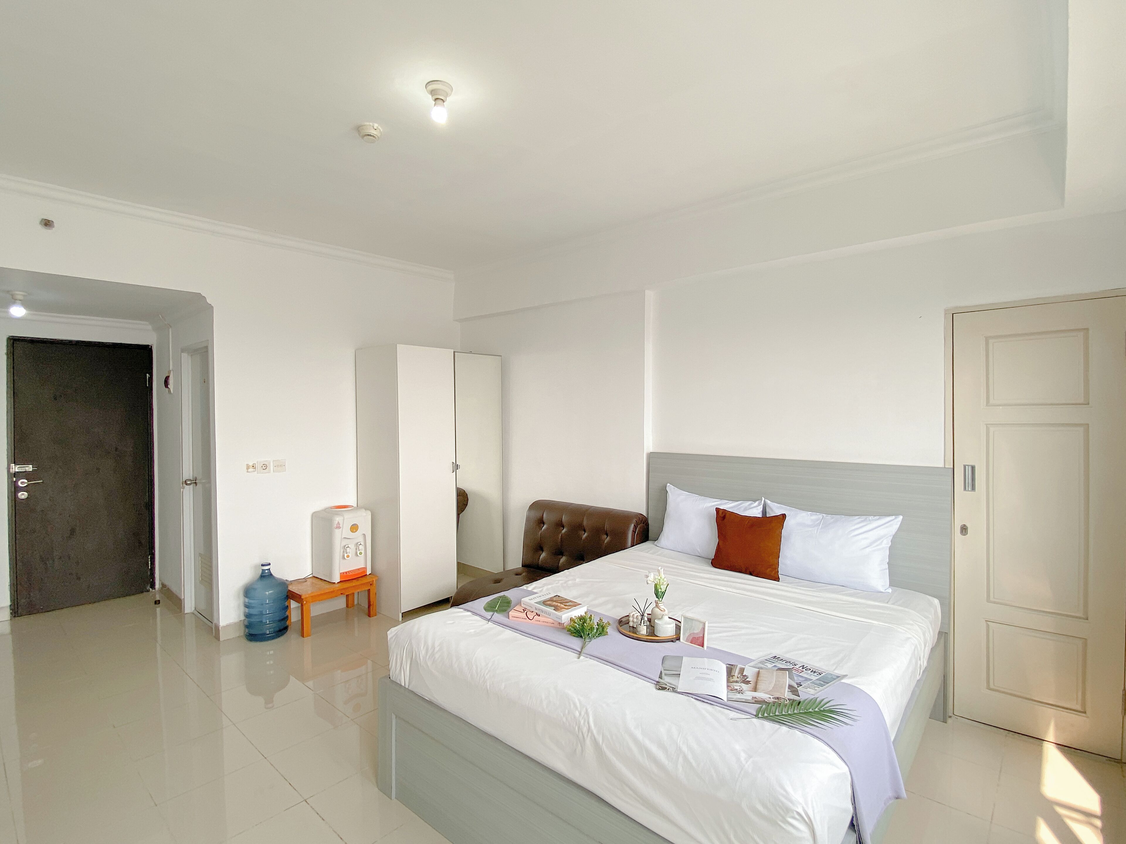 A hotel room with a large bed, a wardrobe, a bedside table, and a water dispenser.