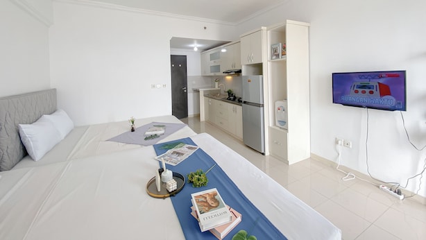 A modern hotel room with a neatly made bed, a small kitchenette, and a television mounted on the wall.