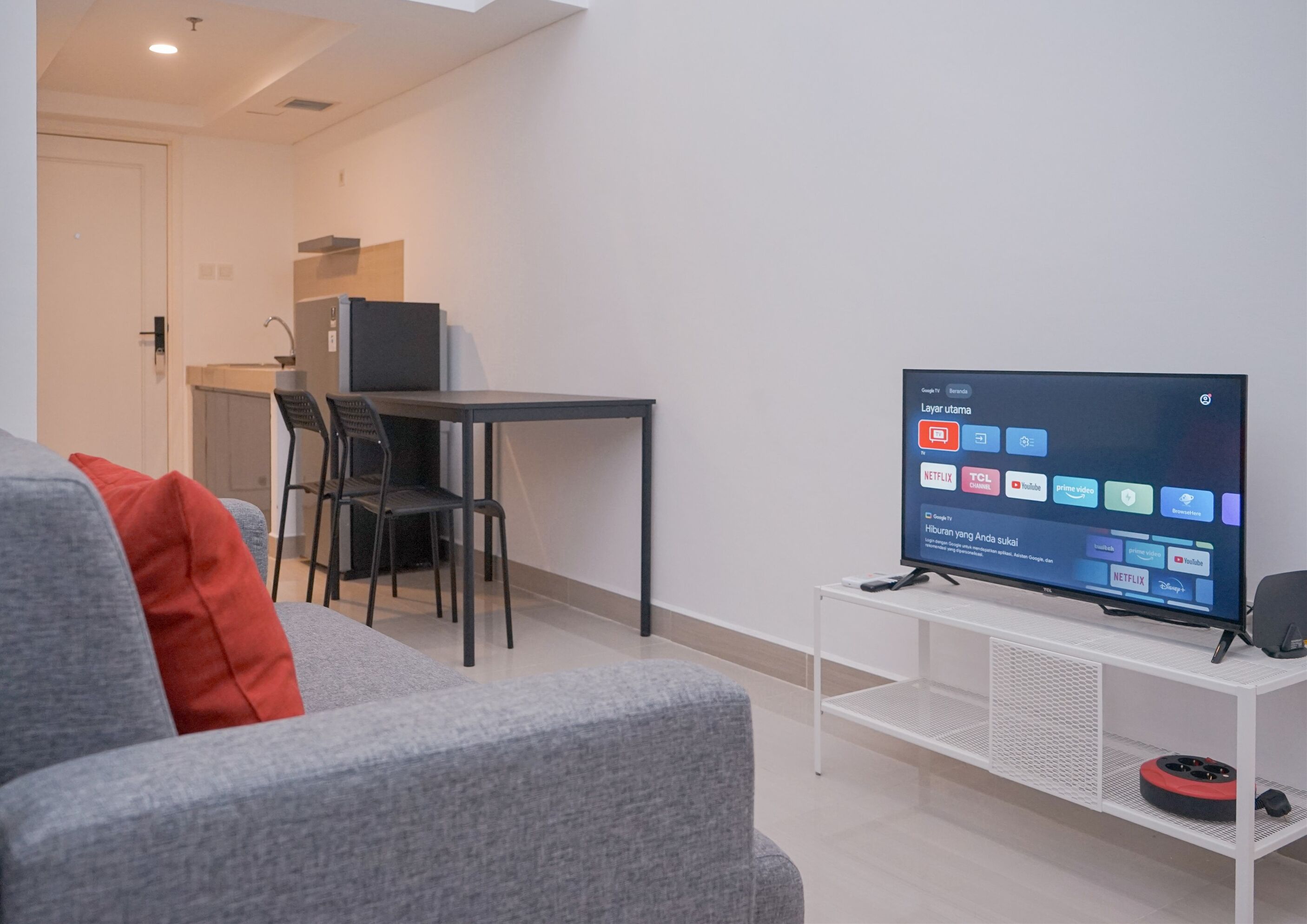 Un salon moderne avec un canapé gris, une petite table et un téléviseur diffusant des services de streaming.