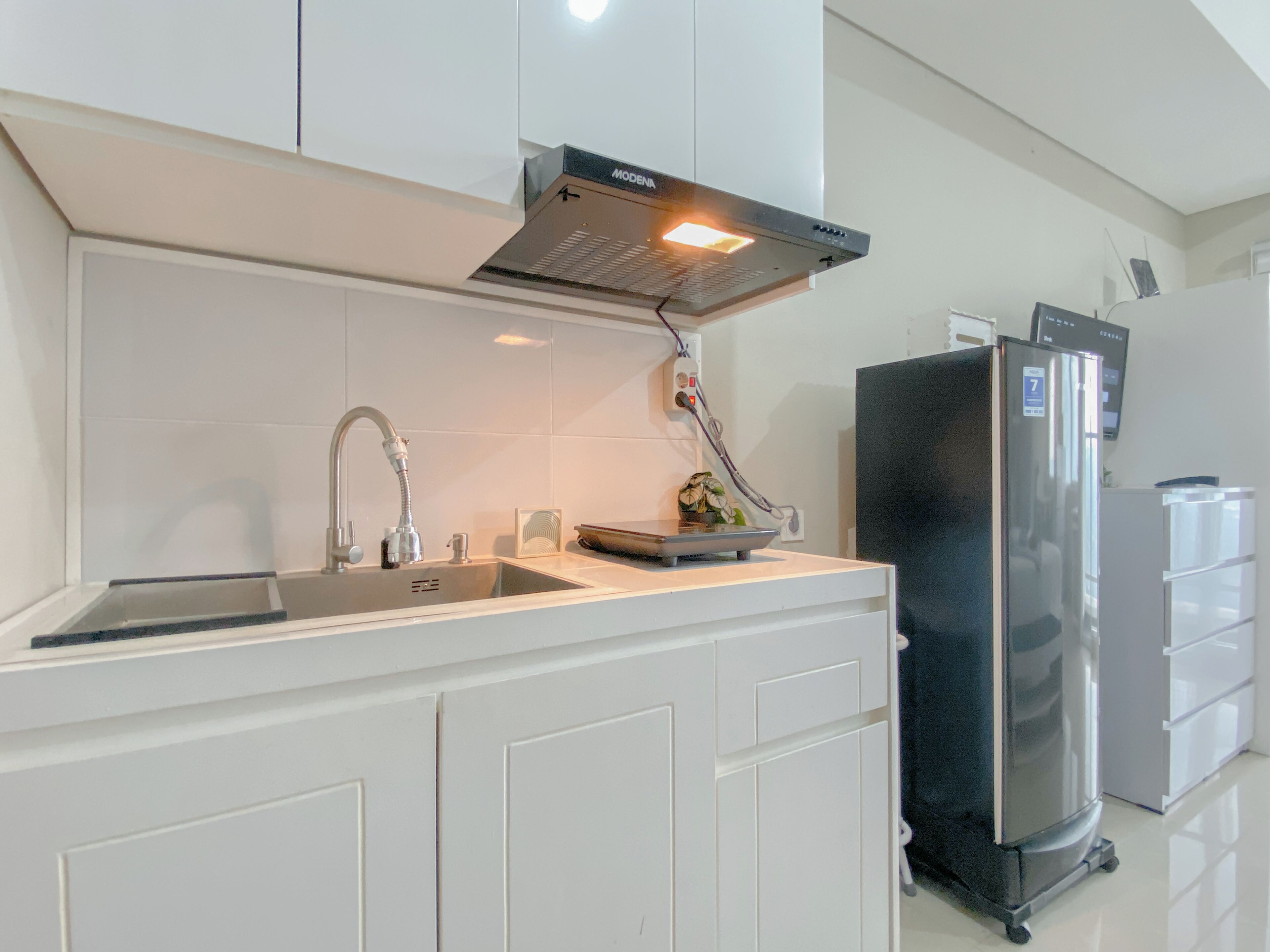 A kitchen with white cabinets, a stainless steel sink, a black refrigerator, and a built-in oven hood.