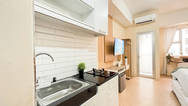 Une cuisine moderne avec des carreaux de céramique blancs disposés en motif métro, un plan de travail noir et un évier en acier inoxydable. On aperçoit une petite plante en pot sur le plan de travail et un téléviseur à écran plat fixé au-dessus.