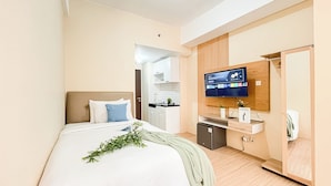 Une chambre d’hôtel avec un lit, un téléviseur fixé au mur, une petite kitchenette et une armoire en bois.