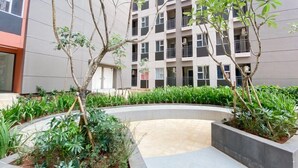 Une cour aménagée avec un chemin sinueux, bordée de verdure et d’arbres, devant un immeuble à plusieurs étages doté de balcons.