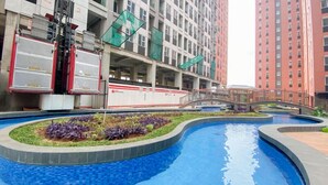 Une piscine avec un pont, entourée d’espaces aménagés et de bâtiments modernes.