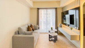 A modern living room with a sofa, a coffee table, and a flat-screen TV mounted on the wall. - Modern Look And Restful 3Br At Meikarta Apartment (Cikarang)