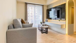 A modern living room with a grey sofa, a small round table, and a TV mounted on the wall. - Modern Look And Restful 3Br At Meikarta Apartment (Cikarang)
