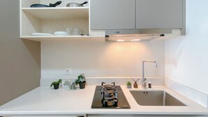 A modern kitchen with white cabinetry, a built-in dishwasher, a stove, and a sink. - New Furnished Studio At Apartment Gold Coast (Jakarta)