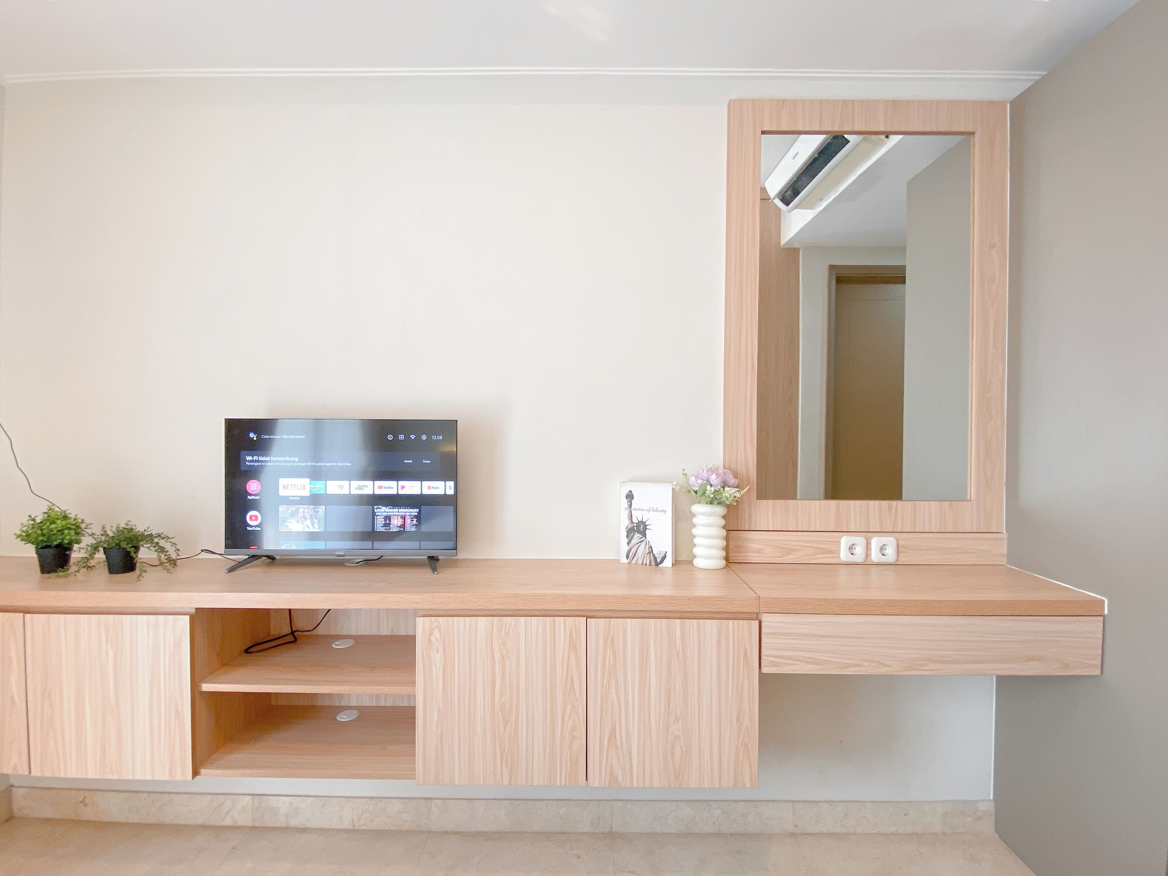 Una habitación moderna y minimalista con un escritorio de madera, un televisor de pantalla plana, una pequeña planta en maceta y un espejo.