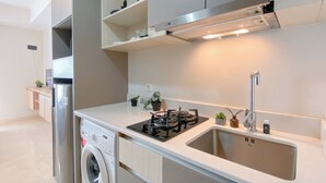 A modern kitchen with a built-in washer, a gas stove, and a stainless steel sink. - New Furnished Studio At Apartment Gold Coast (Jakarta)
