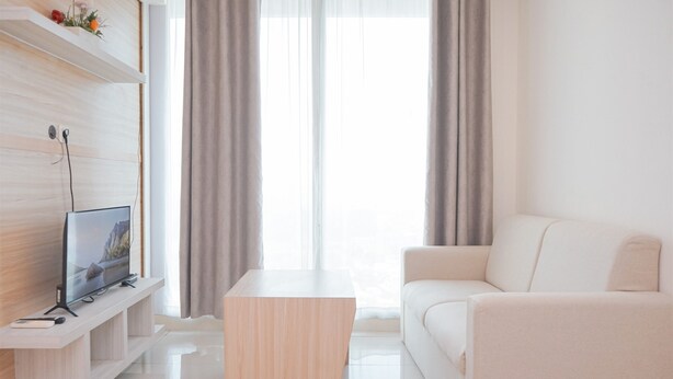 A modern living room with a flat-screen TV on a wooden stand, a white sofa, a wooden coffee table, and a large window with sheer curtains. - Modern Look And Homey 2Br Apartment Tree Park City Bsd (South Tangerang)
