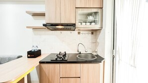 A compact kitchen with a black countertop, a stainless steel sink, a gas stove, and wooden cabinets. - Warm And Comfy 2Br At Bassura City Apartment (Jakarta)