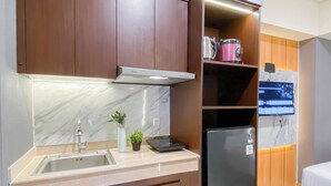 A modern kitchen with a stainless steel refrigerator, a built-in oven, a microwave, and a sink. There is a small potted plant on the counter.