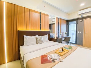 Een hotelkamer met een groot bed, een bureau en een stoel. Er is een raam met gordijnen, een deur en een airconditioning op de muur.