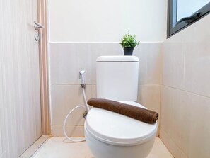 Eine weiße Toilette mit einem braunen Handtuch darauf, einer kleinen Topfpflanze auf dem Tank und einem weißen Rohr, das an der Wand befestigt ist.