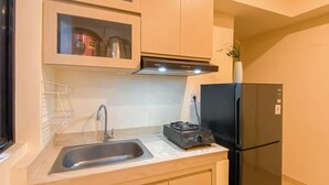 A kitchen with a sink, a stove, a black refrigerator, and wooden cabinets. - Good Deal And Comfy 2Br Apartment Meikarta (Cikarang)