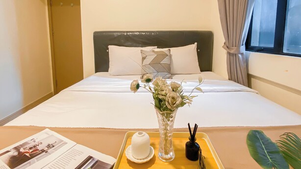 A hotel room with a bed, a tray with a vase of flowers, a magazine, and a bottle of perfume. - Good Deal And Comfy 2Br Apartment Meikarta (Cikarang)