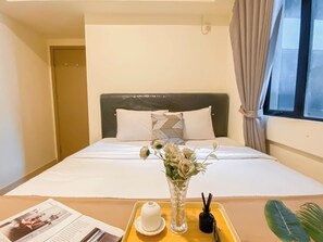 A hotel room with a bed, a tray with a vase of flowers, a magazine, and a bottle of perfume. - Good Deal And Comfy 2Br Apartment Meikarta (Cikarang)