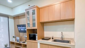 A modern kitchen with wooden cabinets, a built-in microwave, a sink, and a flat-screen TV mounted on the wall. - Cozy And Minimalist 1Br With Working Room Meikarta Apartment (Cikarang)