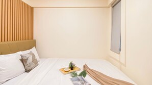 A neatly made bed with white linens, a wooden headboard, and a window with a view. - Cozy And Minimalist 1Br With Working Room Meikarta Apartment (Cikarang)