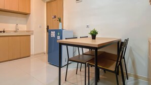 A small, clean kitchen with wooden cabinets, a blue refrigerator, and a dining table with four chairs. - Cozy And Minimalist 1Br With Working Room Meikarta Apartment (Cikarang)